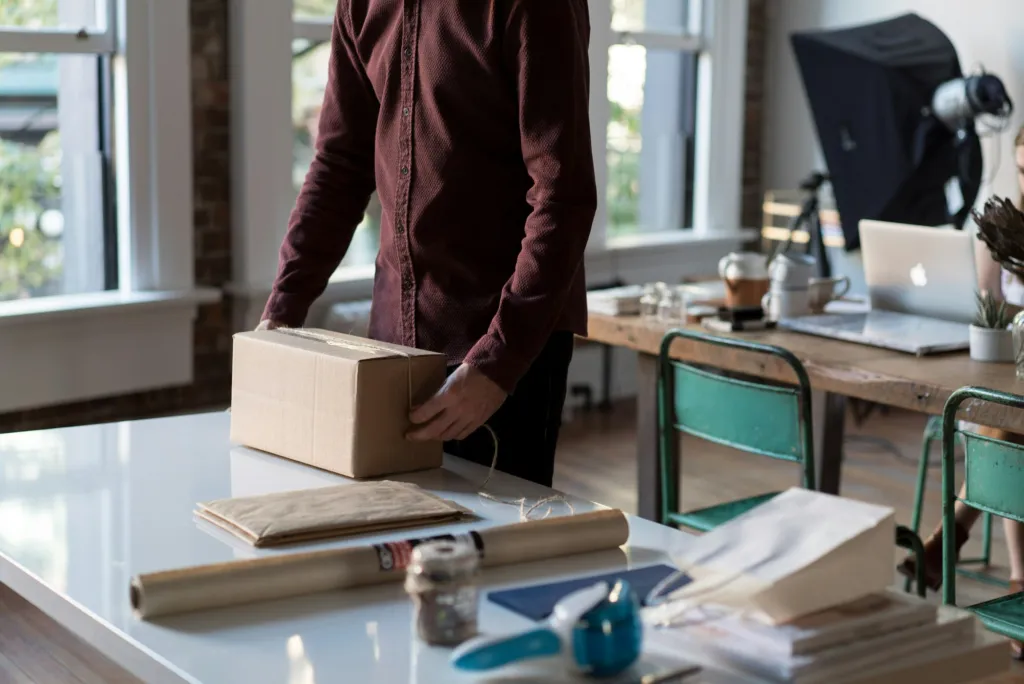 Person packar en kartong på ett kontor med dator i bakgrunden